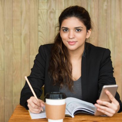 Portrait of young Caucasian female student sitting at desk, doing homework and networking on smartphone